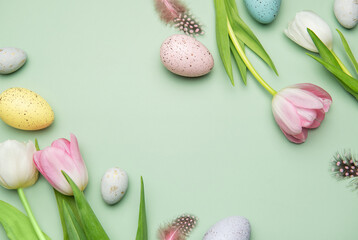 Easter eggs and tulips creating a frame on pastel green background