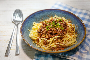 Spaghetti with Bolognese minced meat sauce in a blue plate, napkin and cutlery on a white-painted...
