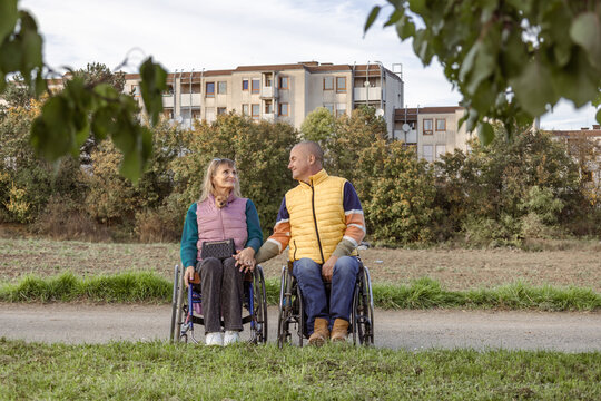 Two people with disabilities in wheelchairs are holding hands