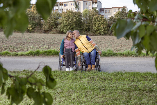 Two people with disabilities in wheelchairs are holding hands