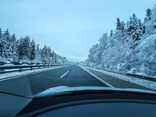 Point-of-view shot from a car driving on a clear highway surrounded by snow-covered trees and winter scenery. 