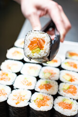 tongs holding sushi hand roll