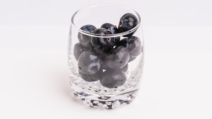 Fresh Black Grapes in a Transparent Glass Cup on a White Background