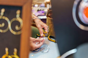 Close up of artisan's hands working with pliers and aluminum wire, creating handmade earrings at a bustling street stall