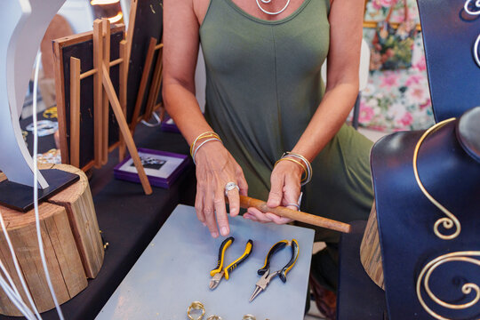 Artisan working aluminum wire with pliers and wooden tools, crafting earrings at her street stall selling handmade jewelry