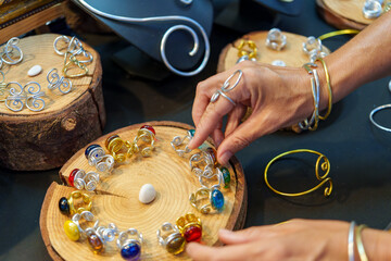 Close up of craftswoman arranging colorful aluminum wire rings with glass beads on wooden display...