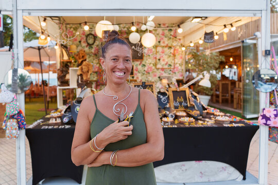Successful hispanic craftswoman in her 50s smiling and posing in her street stall selling handmade aluminum wire jewelry