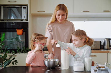 Mother and daughters mixing flour in kitchen, covered in flour, wearing pajamas