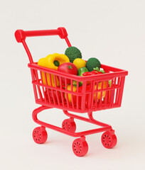 A red plastic toy shopping cart filled with miniature fruits and vegetables against a white background