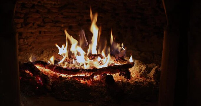 Close-up shot of a warm, crackling fire burning inside a rustic brick oven. Glowing logs and dancing flames create a cozy, traditional atmosphere.