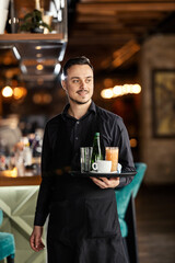 Portrait of professional waiter bringing beverage and refreshment in bar.