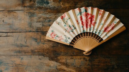 A silk fan with delicate floral patterns resting on a wooden table