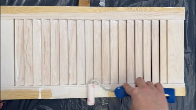 Applying a white paint with a poller to a wooden louvered door. HD footage