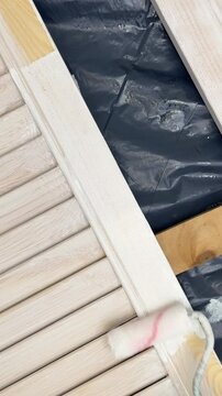 Applying a white paint with a poller to a wooden louvered door, close-up. HD footage