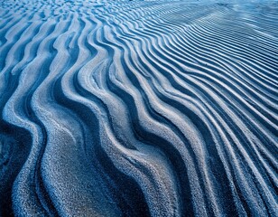 close up of sand ripples with a dusting of frost creating a textured and wavy pattern the contrast between dark sand and icy blue tones highlights natural formations