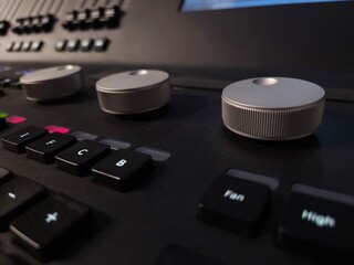 Close-up of a professional lighting control panel with illuminated buttons, rotary dials, and a...