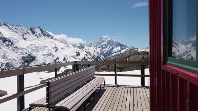 Wooden bench and porch with snowy mountains and Mount Sefton in background on a clear sunny summer day in Mueller Hut, Mount Cook National Park, New Zealand.