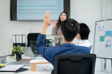 Businessman or male office worker raising a hand to ask a question with female coworker during a meeting