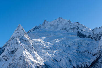 Snow-capped peaks with majestic blue slopes rise above jagged slopes of North Caucasus Range. Mountain tops are covered with eternal glaciers. Dombay. Karachay-Cherkessia.