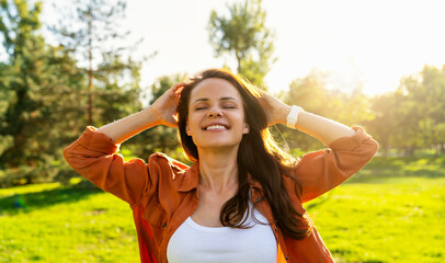 Woman with closed eyes and hands behind head enjoying a walk in a summer park