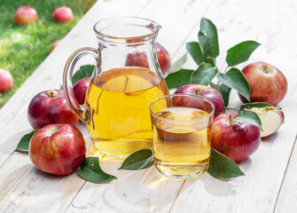 Glass and carafe of fresh apple juice and organic apples on old white wooden table in the garden.