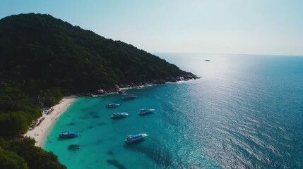 Aerial view of a serene beach with boats near a lush green hill and calm blue waters.