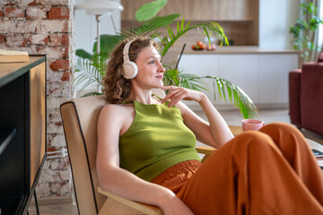 Happy relaxed woman leaning back in comfy chair with headphones enjoy music and positive thoughts....