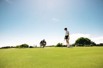 Female golfer in golf attire on putting green with male observer
