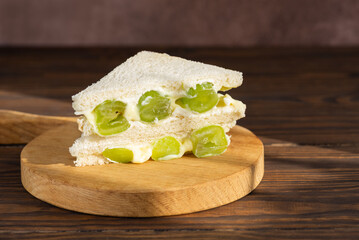 Korean sandwich with green grape and cream cheese on a brown wooden table. Hard light. Asian dessert, street food.