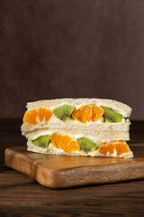 Korean sandwich with kiwi, orange and cream cheese on a wooden board. Hard light. Asian dessert, street food. Vertical orientation.