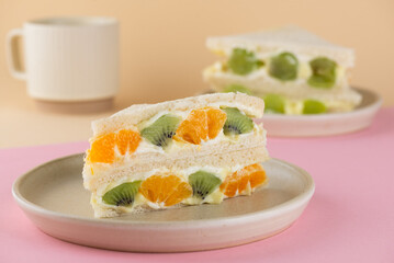 Homemade Korean style bread sandwiches with kiwi, orange, grape and cream cheese with cup of coffee on a beige and pink background.