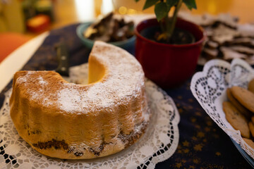 A festive table display featuring a sliced homemade bundt cake dusted with powdered sugar, surrounded by traditional Christmas cookies and holiday treats.