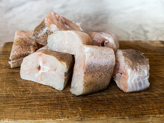 Sliced ​​pieces of raw hake fish on an oak cutting board