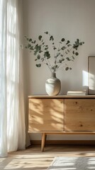 A serene moment in a sunlit room captures a stylish wooden piece adorned with a beautiful vase filled with delicate greenery. Soft curtains gently diffuse the light, creating an inviting atmosphere