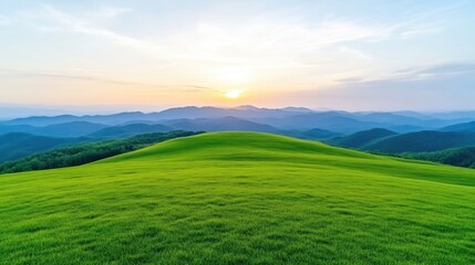 Obraz premium Lush green meadow at mountain peak sunset. Vast expanse of vibrant green grass, rolling hills, and misty mountain ranges in the background, under a serene sunset sky