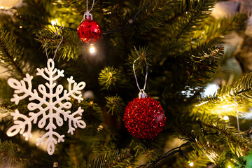 A beautifully decorated Christmas tree with red baubles and a white snowflake ornament captured in a warm, glowing close-up.