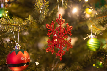 Warm and festive close-up of a decorated Christmas tree featuring a red snowflake ornament, glowing string lights, and colorful baubles. The image captures the joyful spirit and cozy ambiance.