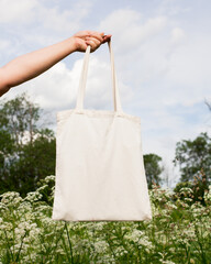 Mature senior woman, female hand holding white eco bag canvas fabric for mock up blank template on...