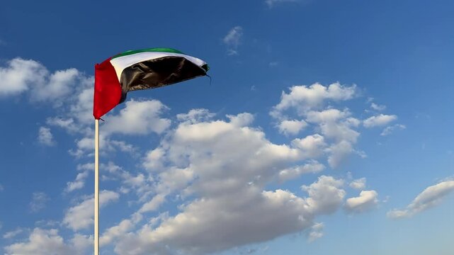 Flag of the UAE waving against the sky. The vibrant flag of the UAE ripples in the breeze, contrasting with the clear sky above. The UAE flag proudly flutters in the wind