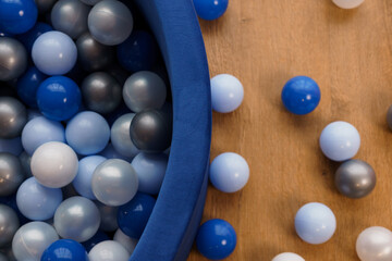 Close-up of colorful plastic balls in shades of blue, gray, and silver inside and around a blue ball pit on wooden floor background