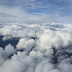 Aerial view of fluffy white clouds and blue sky, captured from an airplane window.