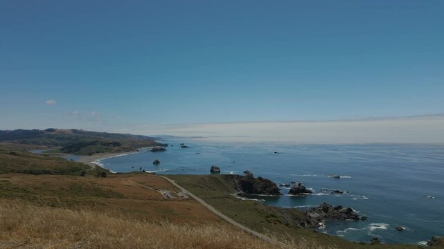 Lush shoreline with road by blue ocean in the Jenner Headlands Preserve under clear sky