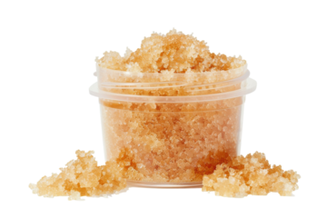 Natural brown sugar scrub in a clear container with scattered grains on a white background
