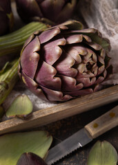 Obraz premium Whole purple raw roman artichokes in a wooden tray closeup. Fresh italian vegetables