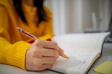 person wearing yellow sweater is writing in notebook with pen, focusing on task. scene conveys...