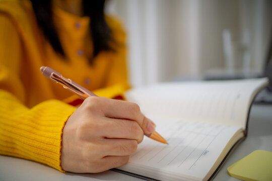 person wearing yellow sweater is writing in notebook with pen, focusing on task. scene conveys sense of productivity and concentration in cozy indoor setting