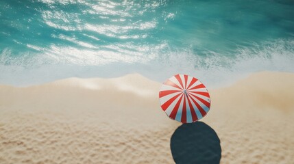 Obraz premium Overhead view of red and white striped beach umbrella on sandy beach near ocean.