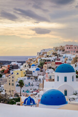 Scenic view of Oia, Santorini, Greece, with blue-domed churches, colorful houses, and the Aegean Sea. Vertical shot with a cloudy sky, a beautiful island for honeymoon travel or wedding destination
