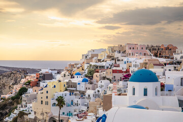 Scenic view of Oia, Santorini, Greece, with blue-domed churches, colorful houses, and the Aegean Sea. Horizontal shot with a cloudy sky, a beautiful island honeymoon or wedding destination