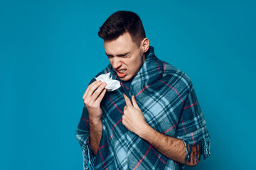 Young guy wrapped in plaid sneezes isolated
